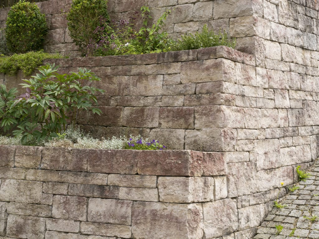 Hellbraune Mauer aus Natursteinen mit Pflanzen