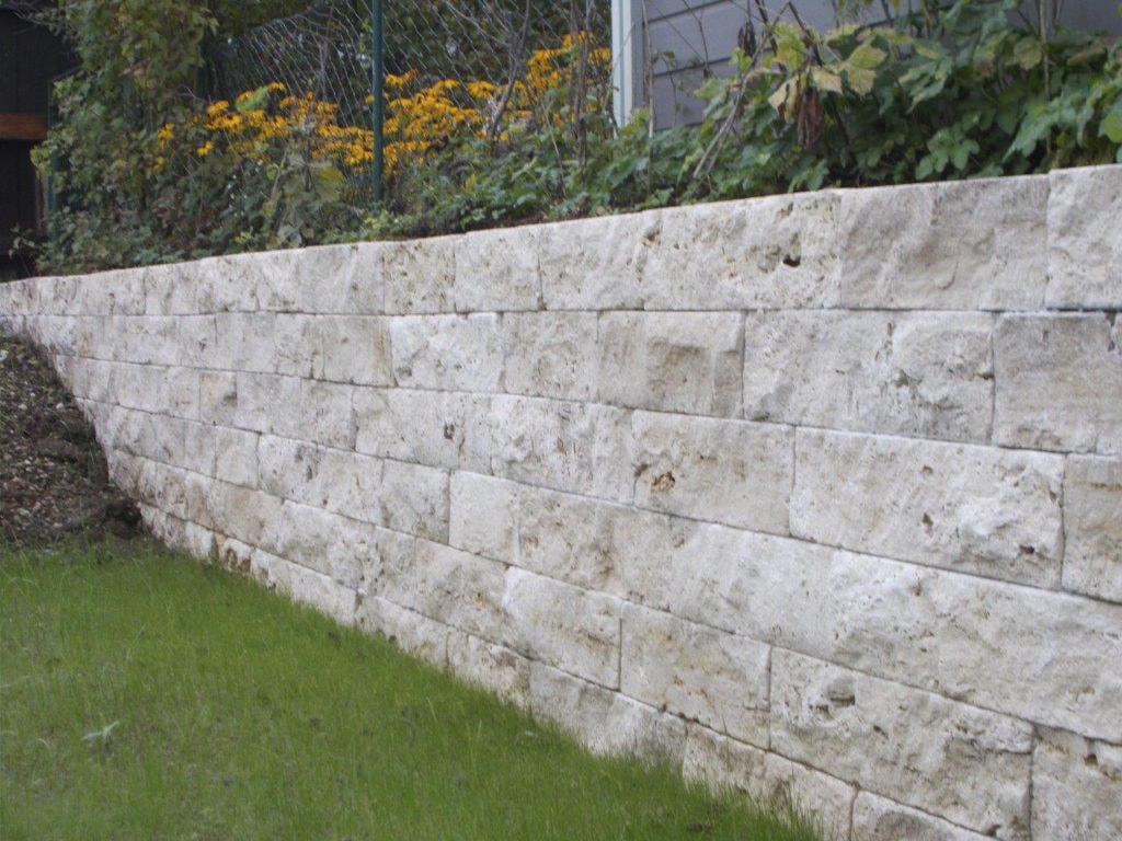 Eine beige Mauer aus Natursteinen mit Pflanzen darauf
