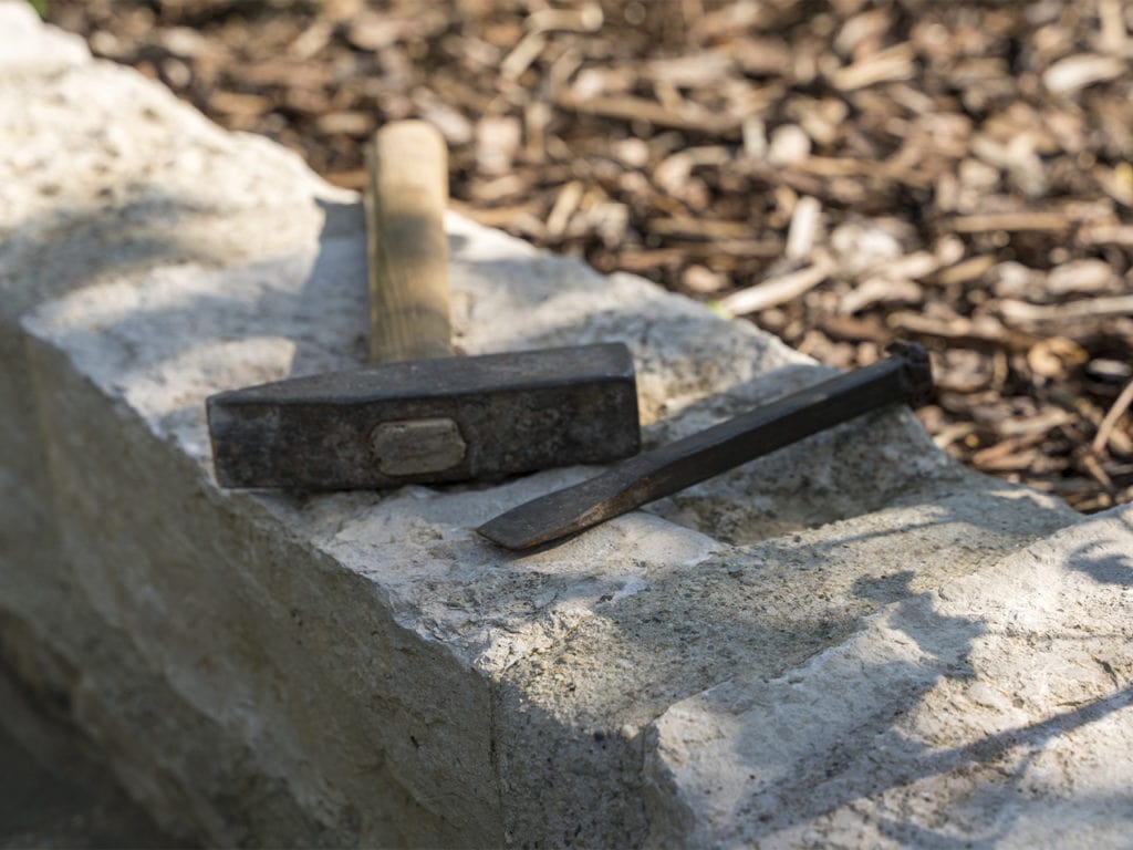 Ein Hammer und ein Meißel liegen auf einer Mauer aus Natursteinen