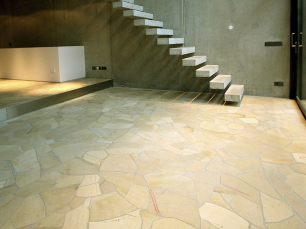 Ein Raum gepflastert mit Polygonalplatten während man im Hintergrund eine Treppe sieht
