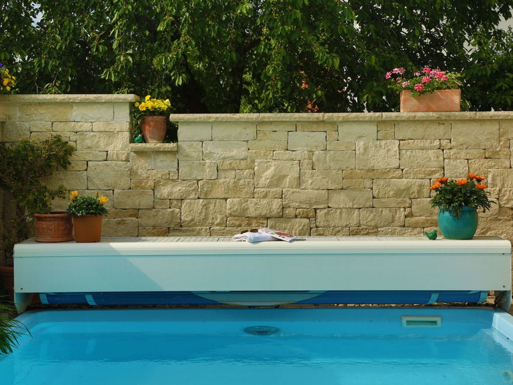 Eine Mauer aus Jura Marmor mit einer Liege und einem Pool im Vordergrund