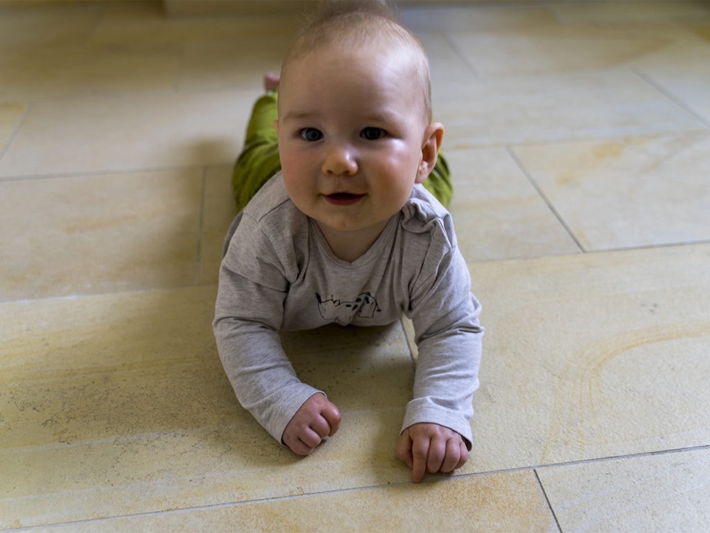 Ein Baby liegt auf Solnhofener Bodenplatten und schaut in die Kamera