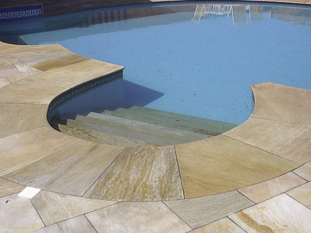 Ein mit Terassenplatten aus Naturstein gepflasterter Pool mit einer in den Pool führenden Treppe